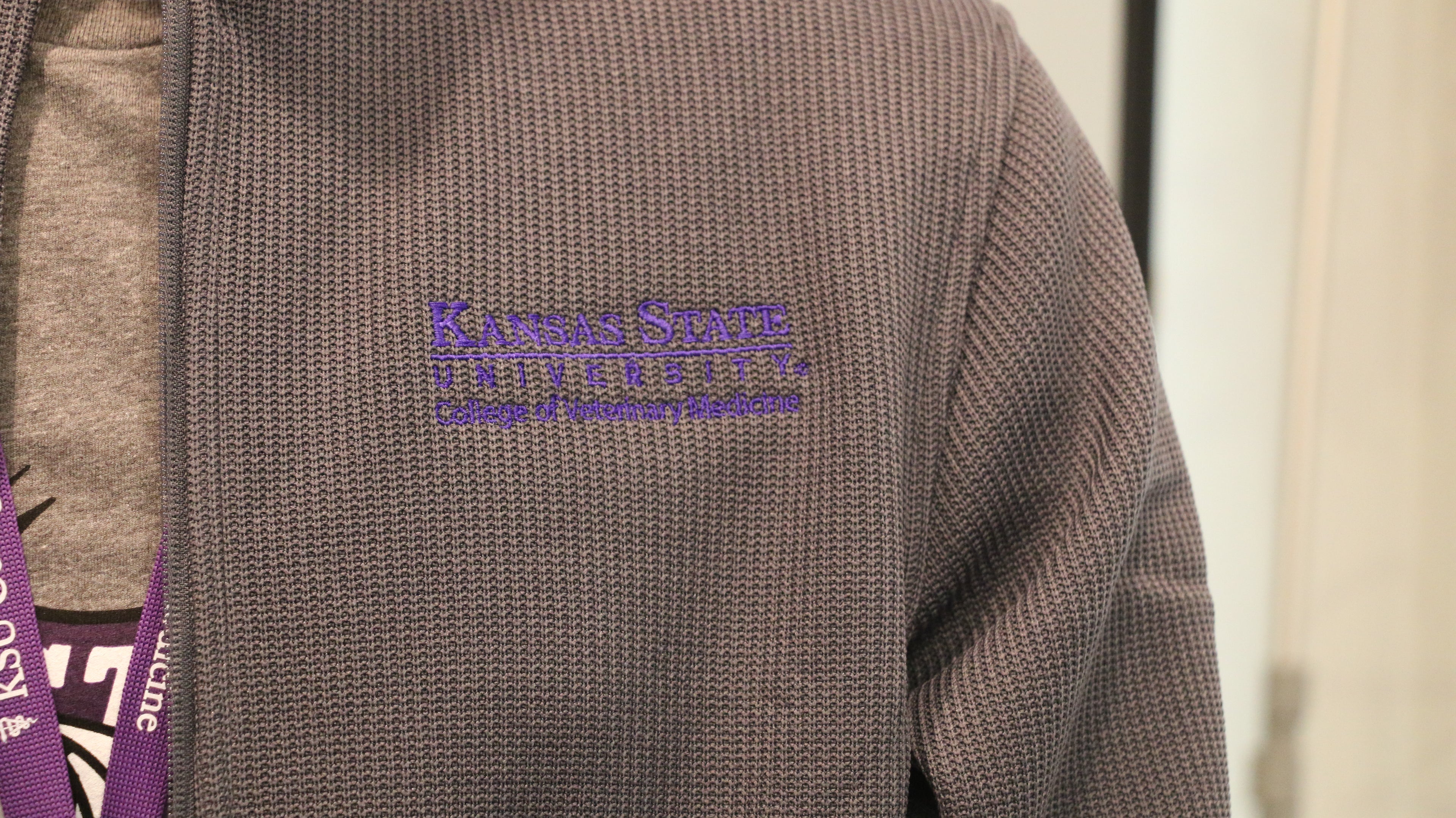A close-up view of the purple embroidered Kansas State University College of Veterinary Medicine logo on the upper left chest area. 