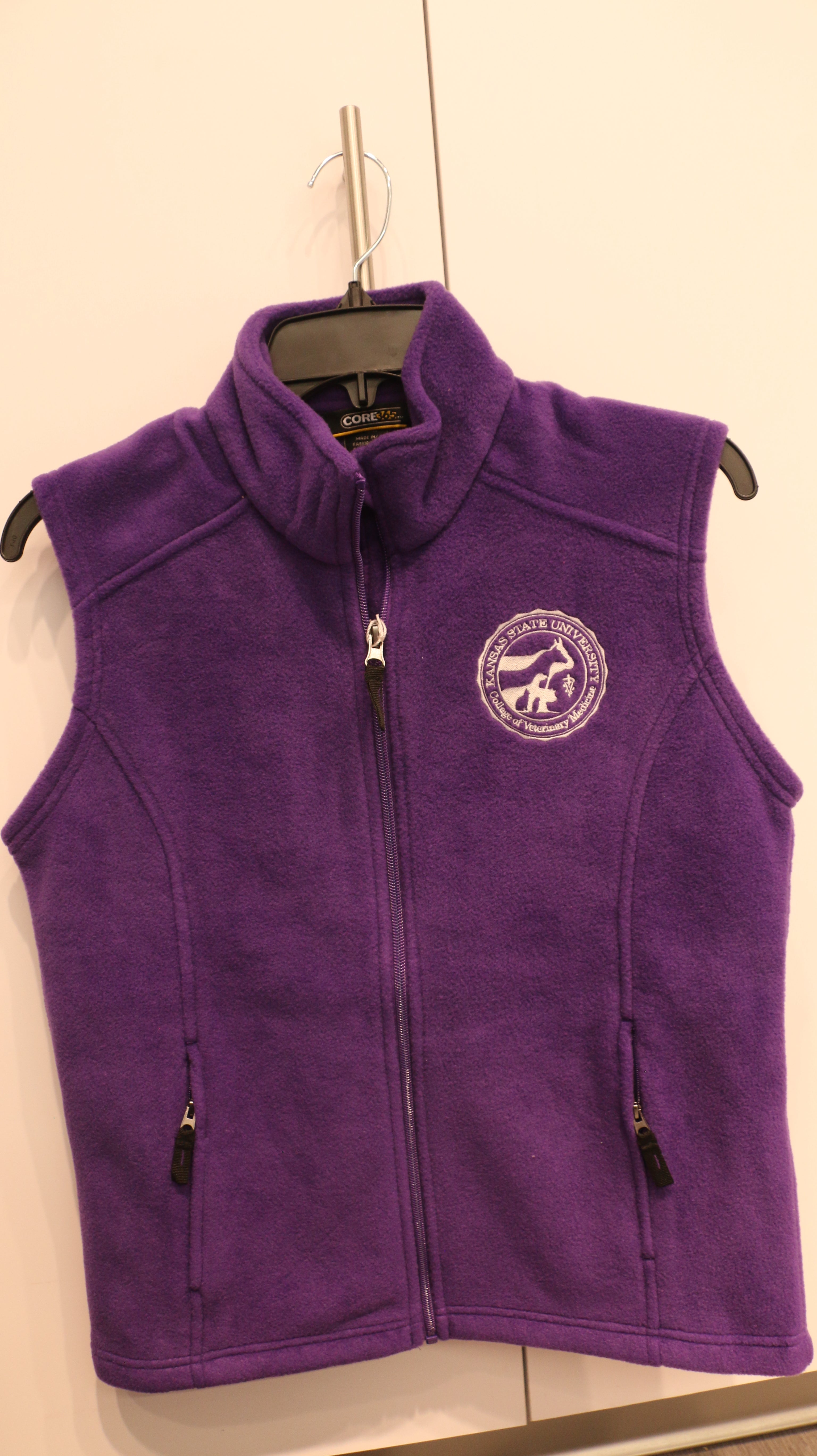 A purple full zip fleece vest with the CVM seal on the front, two zip pockets, displayed on a hanger.