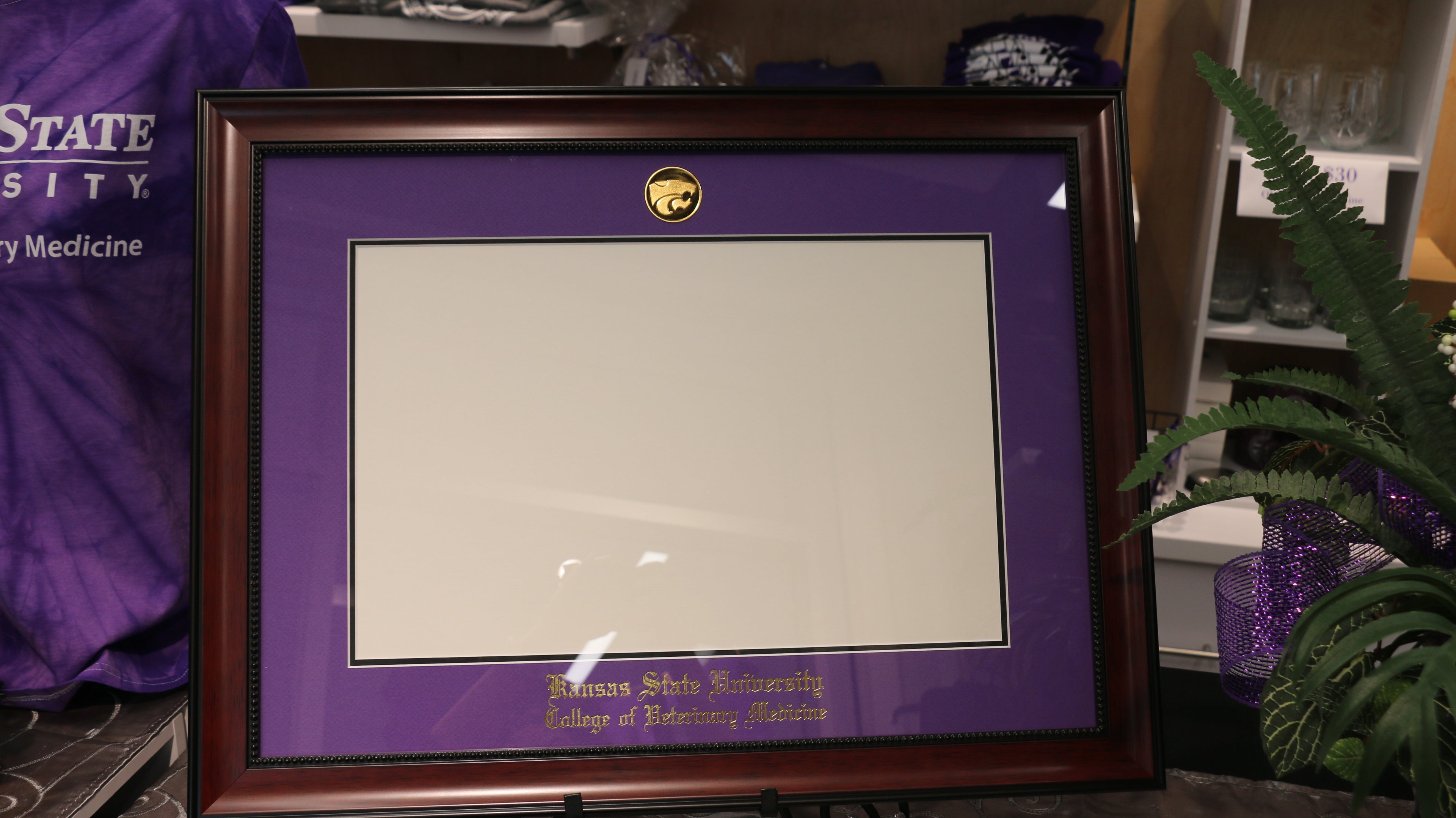 A diploma frame with an avalon mahogany finish, purple primary mat, and black accent mat. It features an imprint of Kansas State University College of Veterinary Medicine and a gold plated power cat logo.
