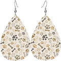 A pair of beige, brown, and black leather earrings with small paws and bones making up the pattern. 