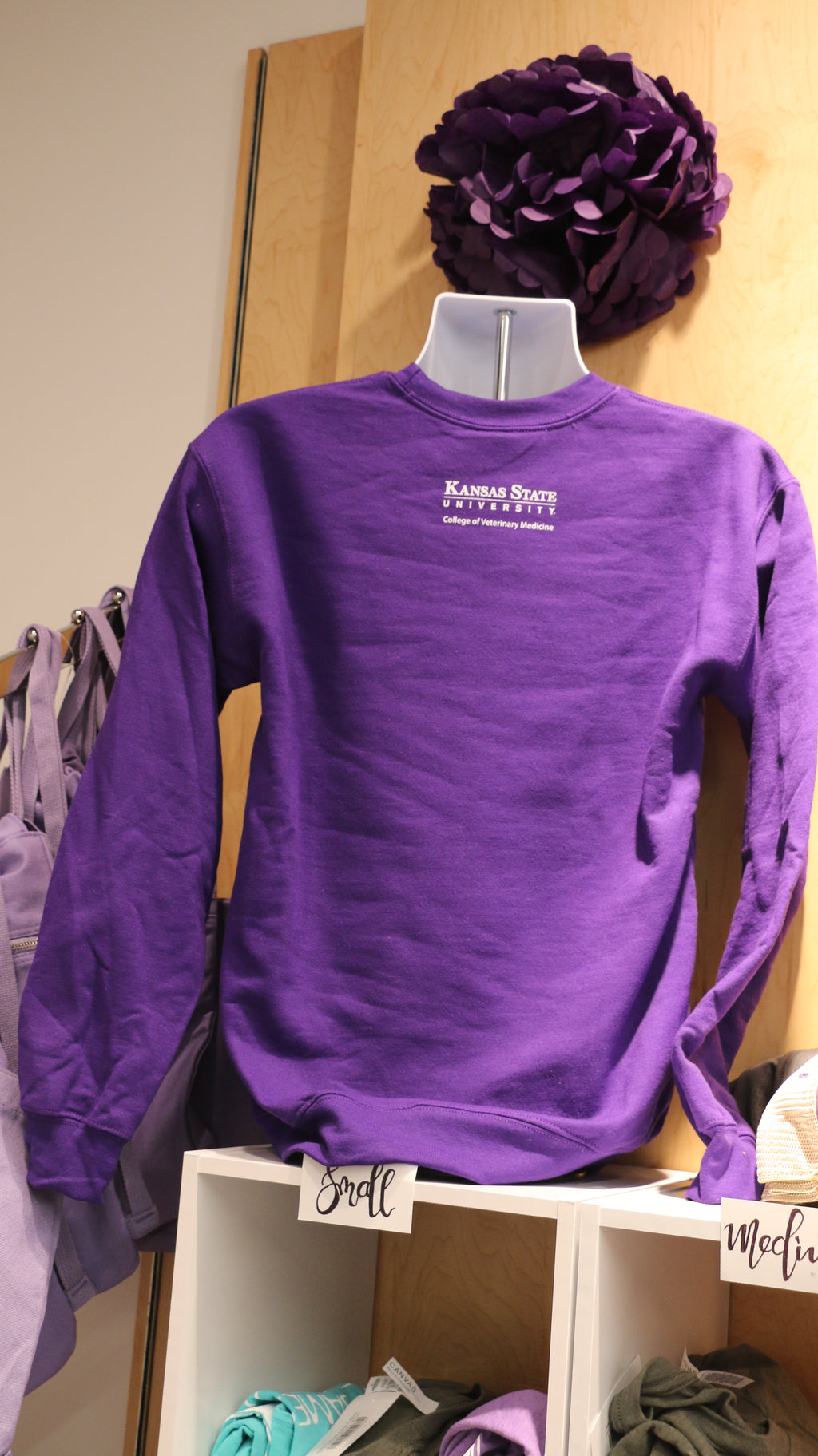 A rear view of the purple sweatshirt with a white CVM logo on the upper middle back area. 