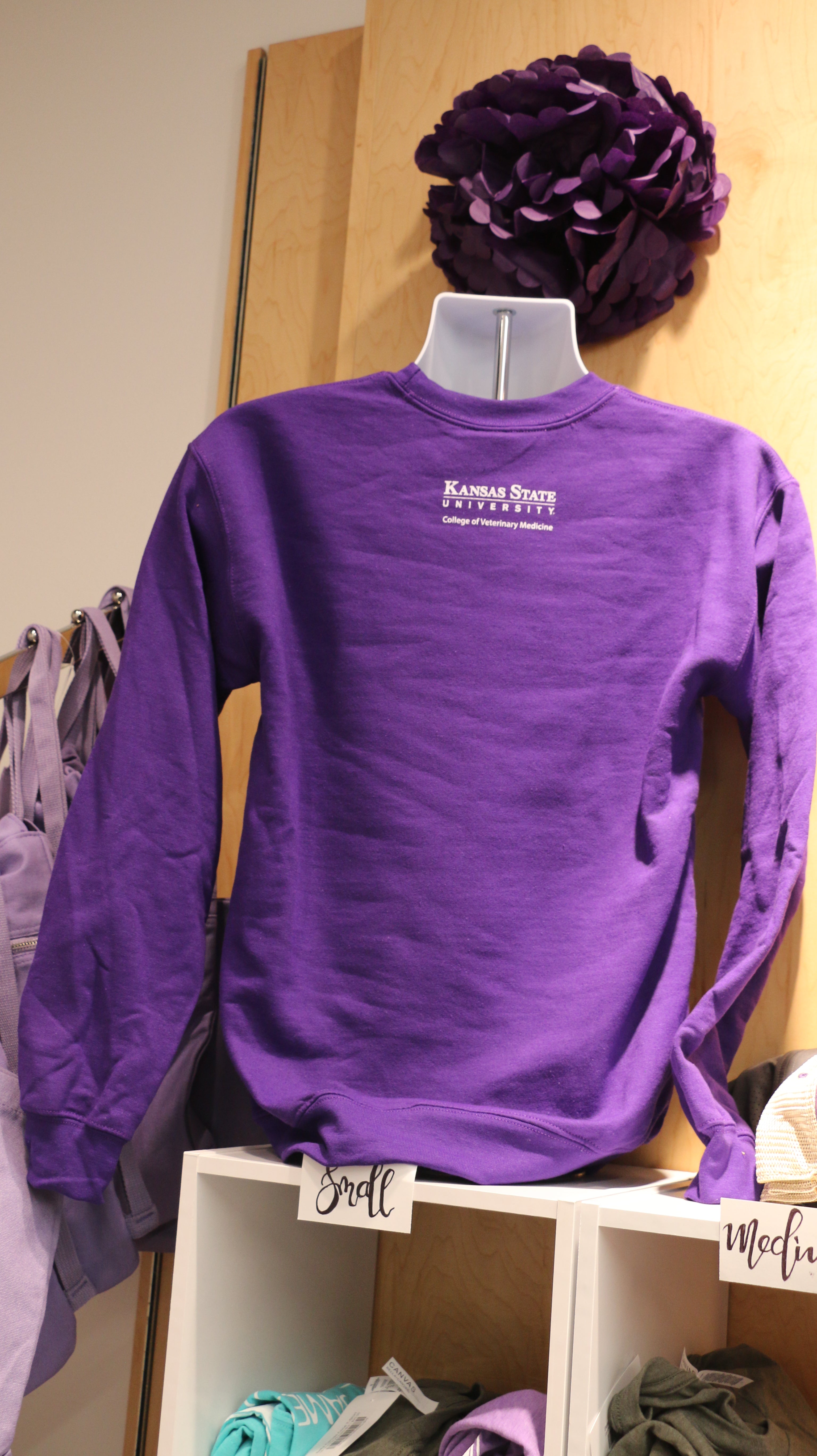 A rear view of the purple sweatshirt with a white CVM logo on the upper middle back area. 