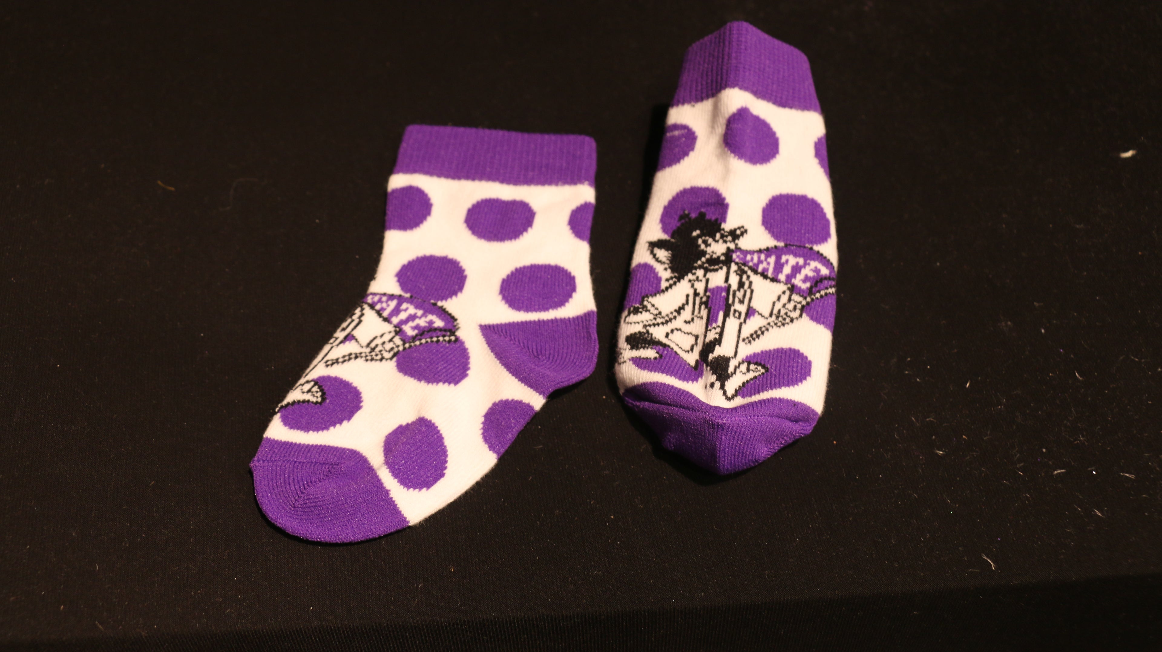 A pair of purple infant socks with a white polka dot pattern and Labcoat Willie. 