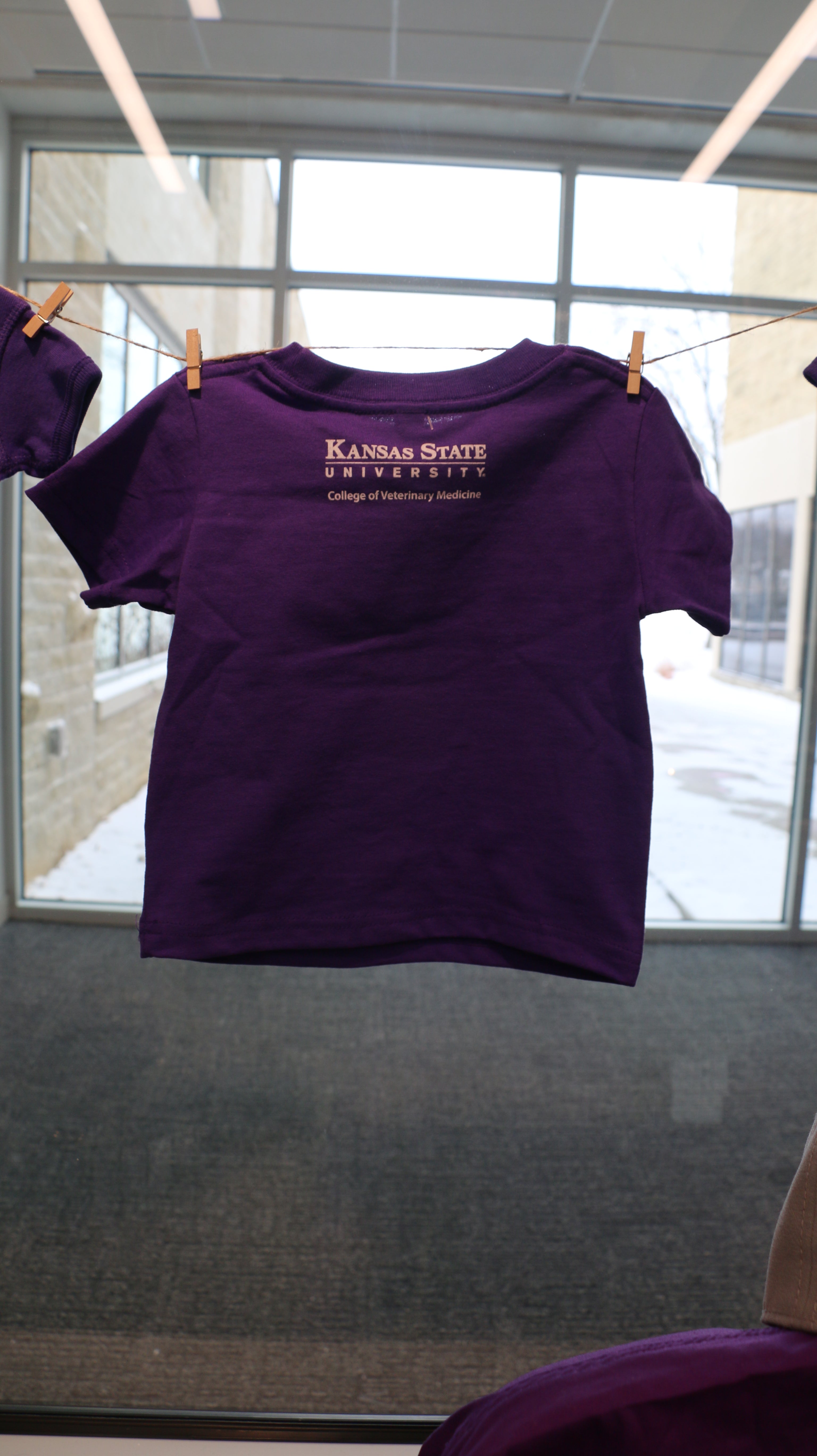 A rear view of the purple short sleeve toddler t-shirt that has a white Kansas State University College of Veterinary Medicine logo in the upper center back area. 