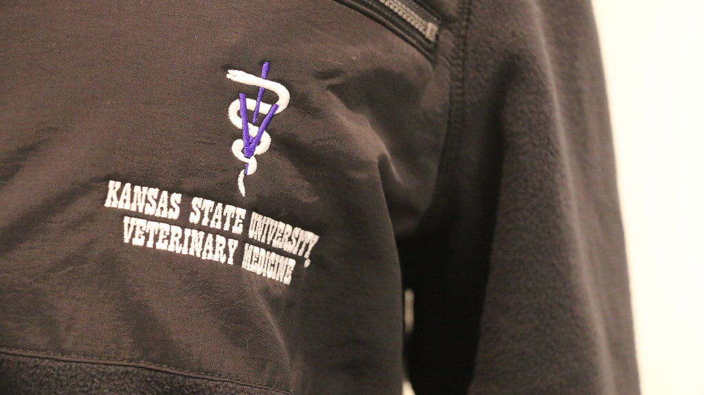 A close-up of the white lettering "Kansas State University Veterinary Medicine" on the upper left chest area. 
