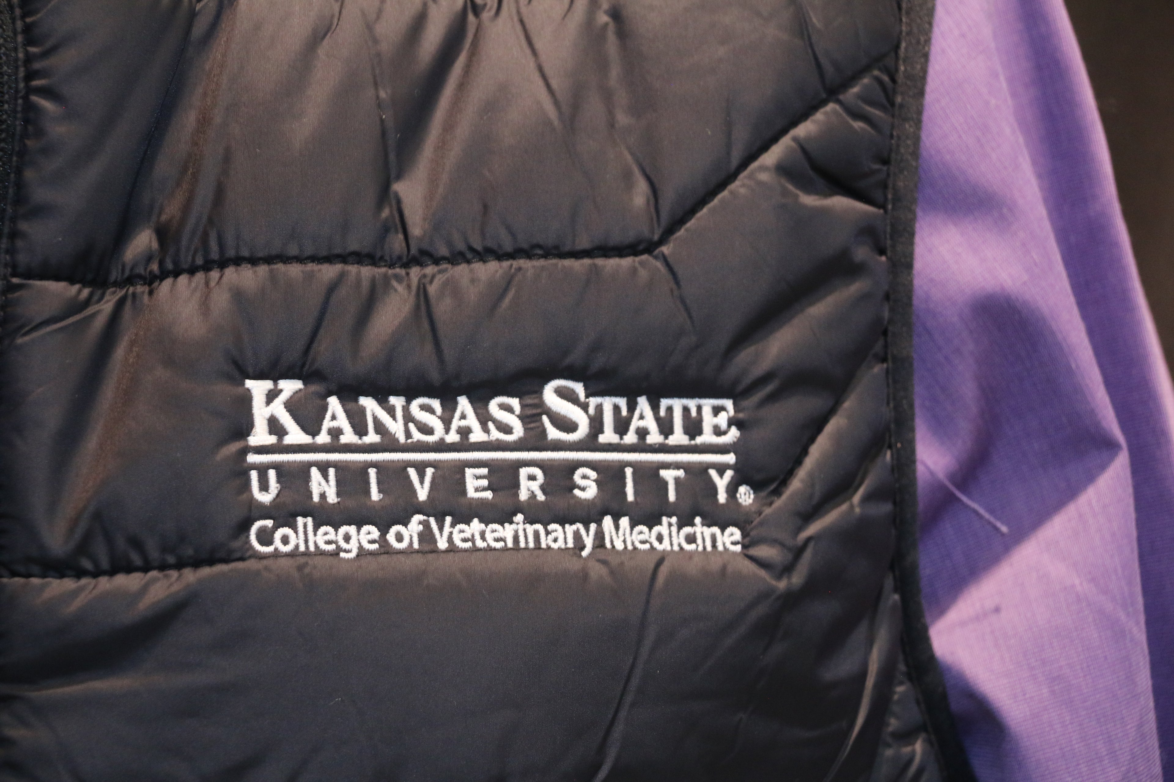 A close-up view of the white K-State logo on the left chest of the puffer vest.