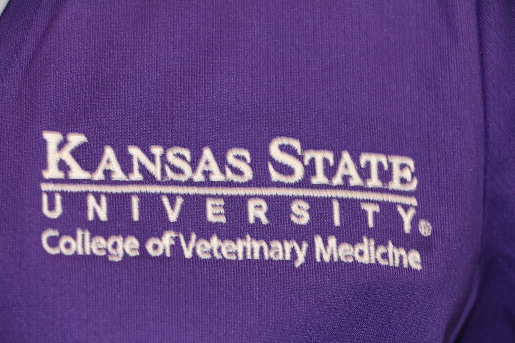A close-up view of the white CVM logo on the top left side of the purple Nike polo. 