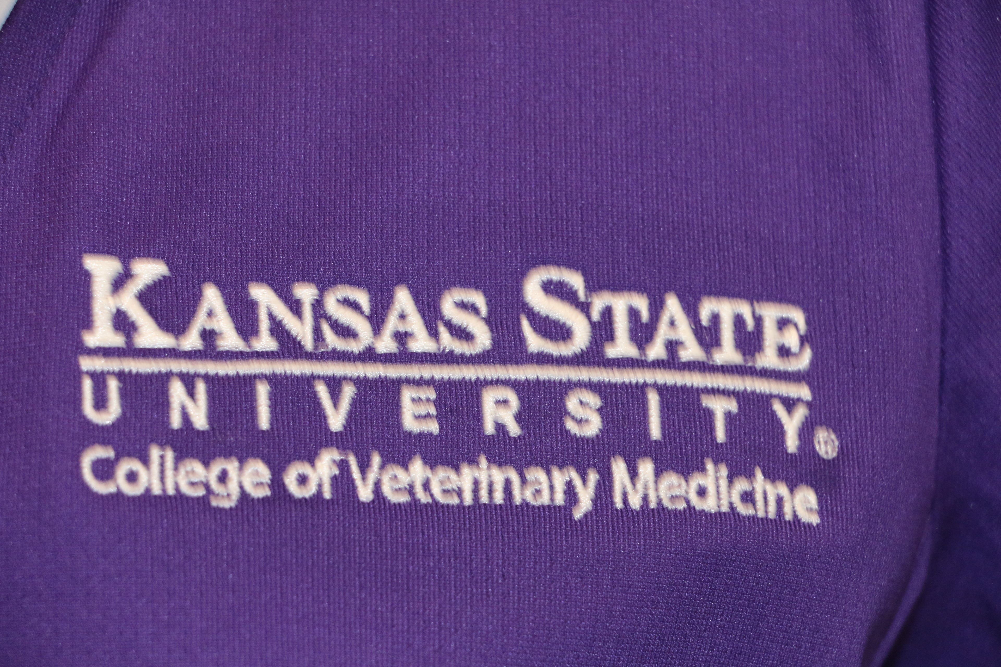 A close-up view of the white CVM logo on the top left side of the purple Nike polo. 