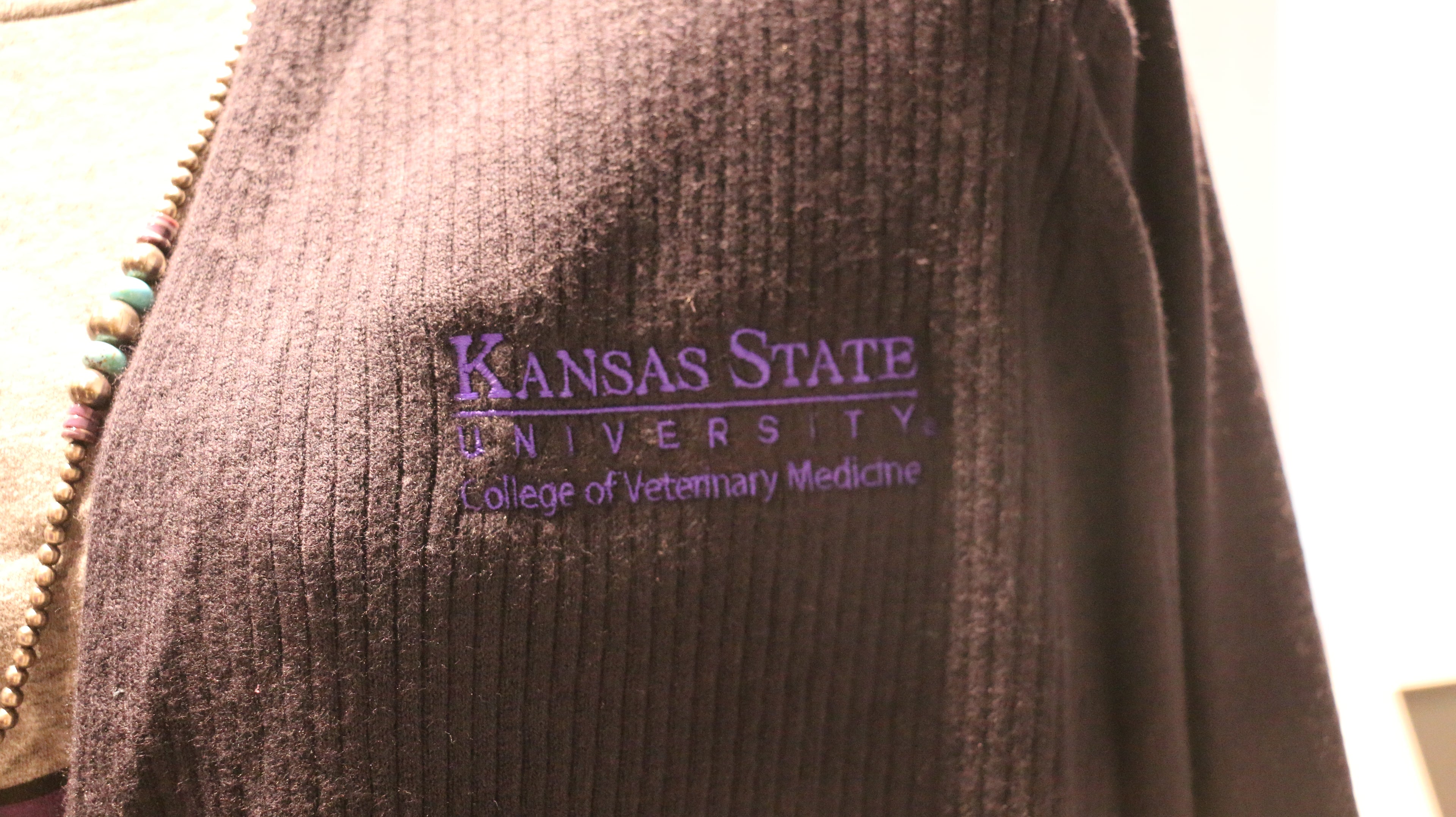 A close-up view of the purple "Kansas State University College of Veterinary Medicine" embroidered on the upper left chest area. 