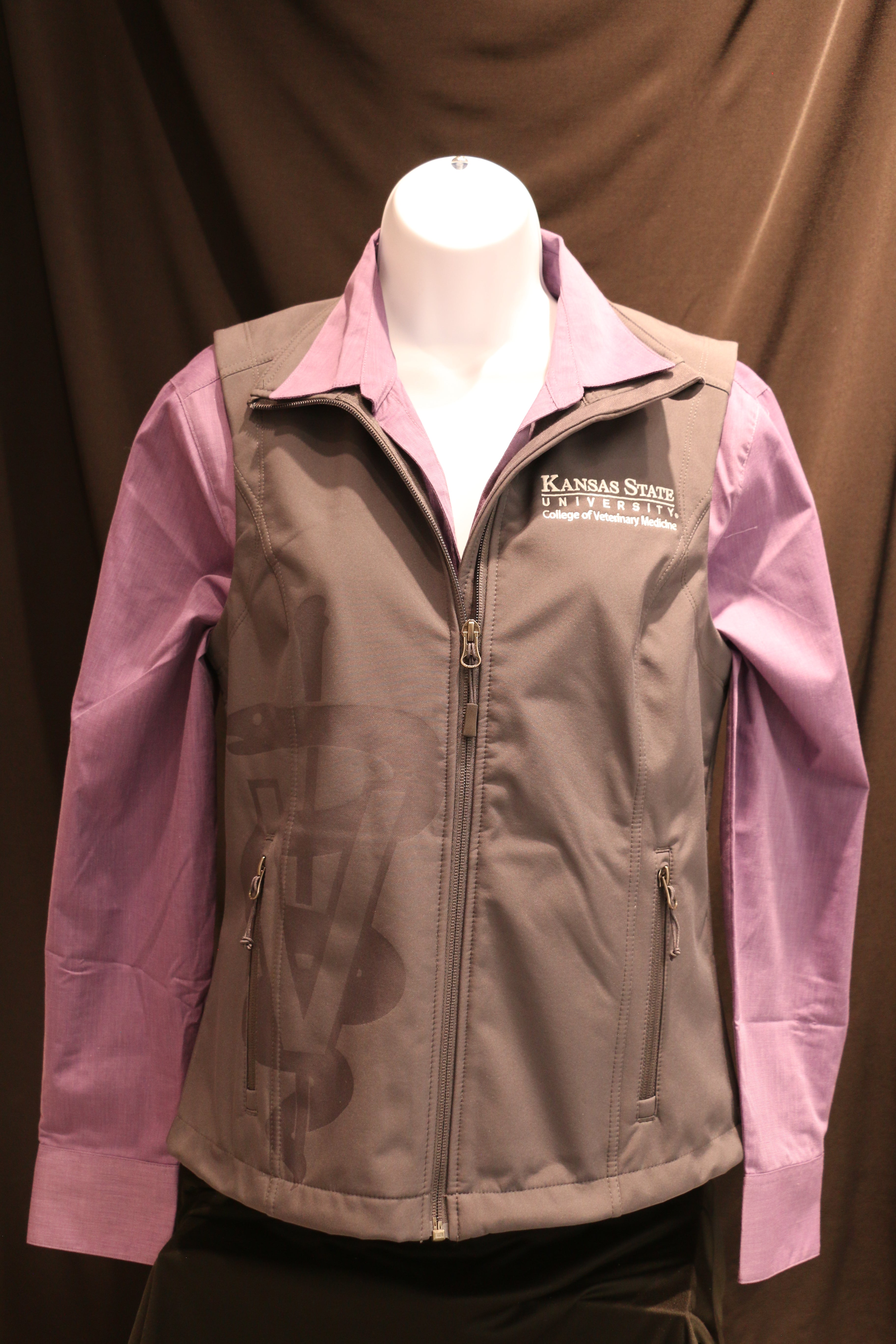 An partially unzipped gray Port Authority lightweight vest for ladies featuring laser caduceus etching, side zip pockets, white CVM logo, and displayed with a purple shirt underneath.