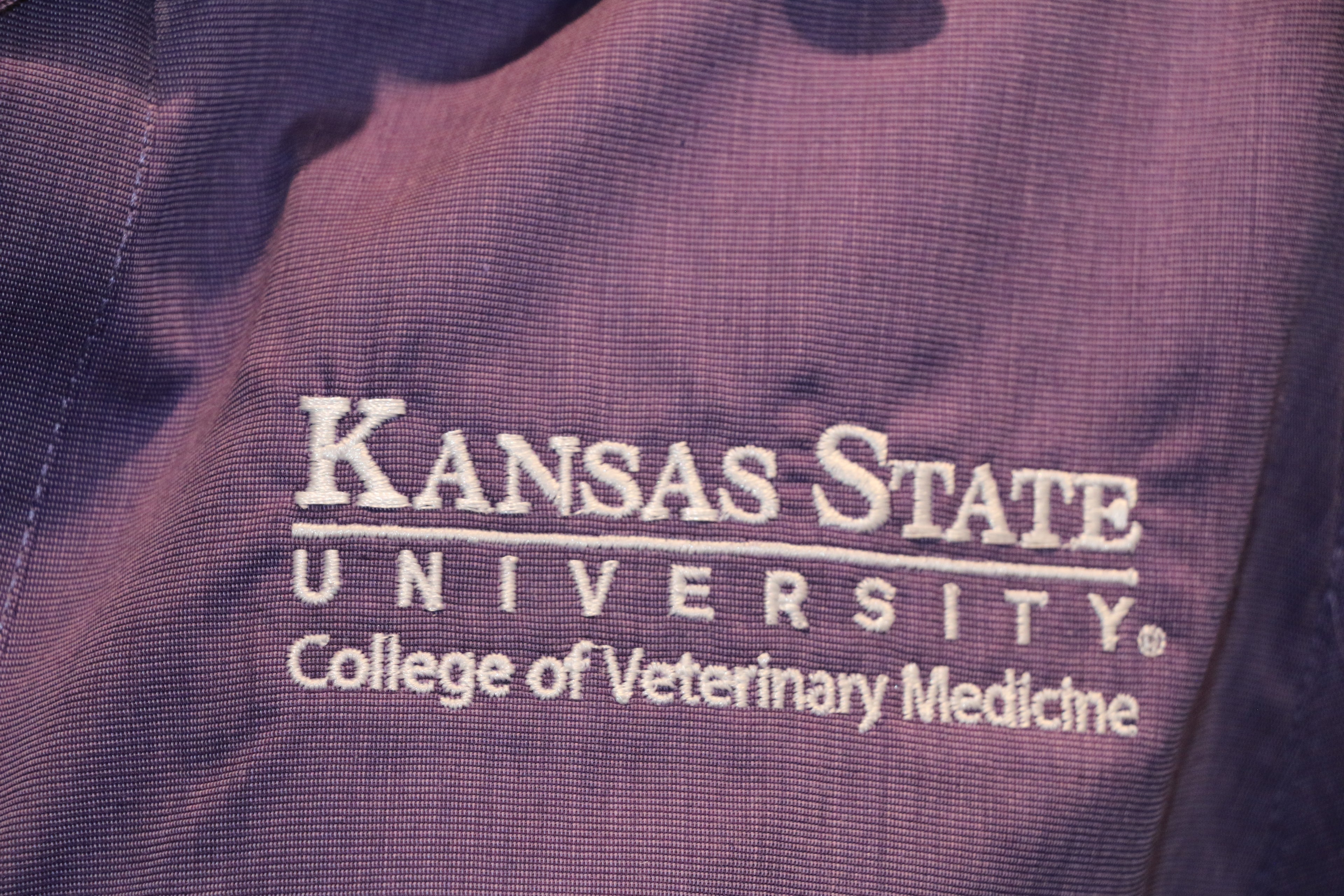 A close up of the customized Port Authority Purple Woven long sleeve button up dress shirt white Kansas State University seal. 