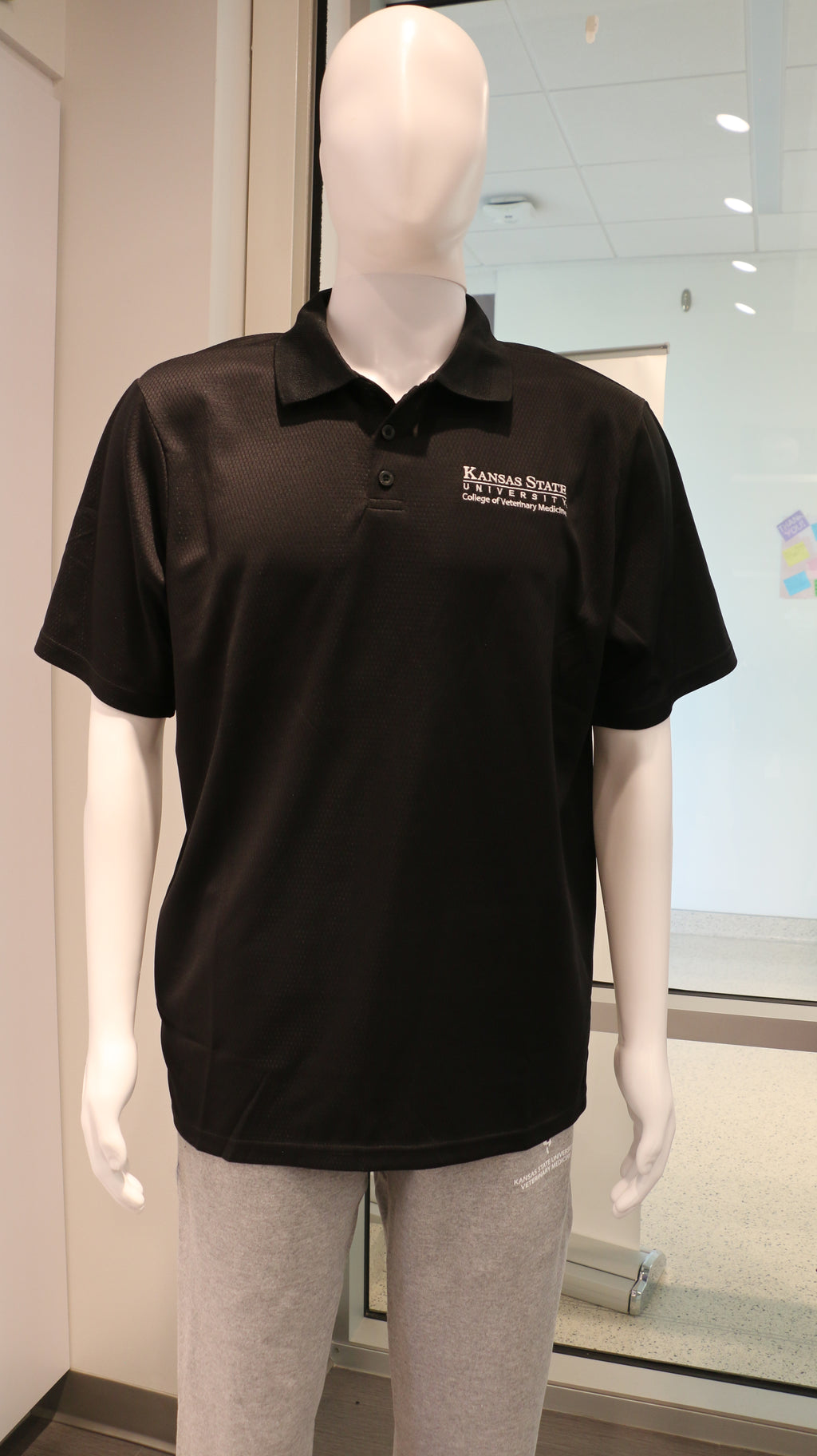 A black Holloway Prism Polo shirt with a white CVM logo displayed on a mannequin.