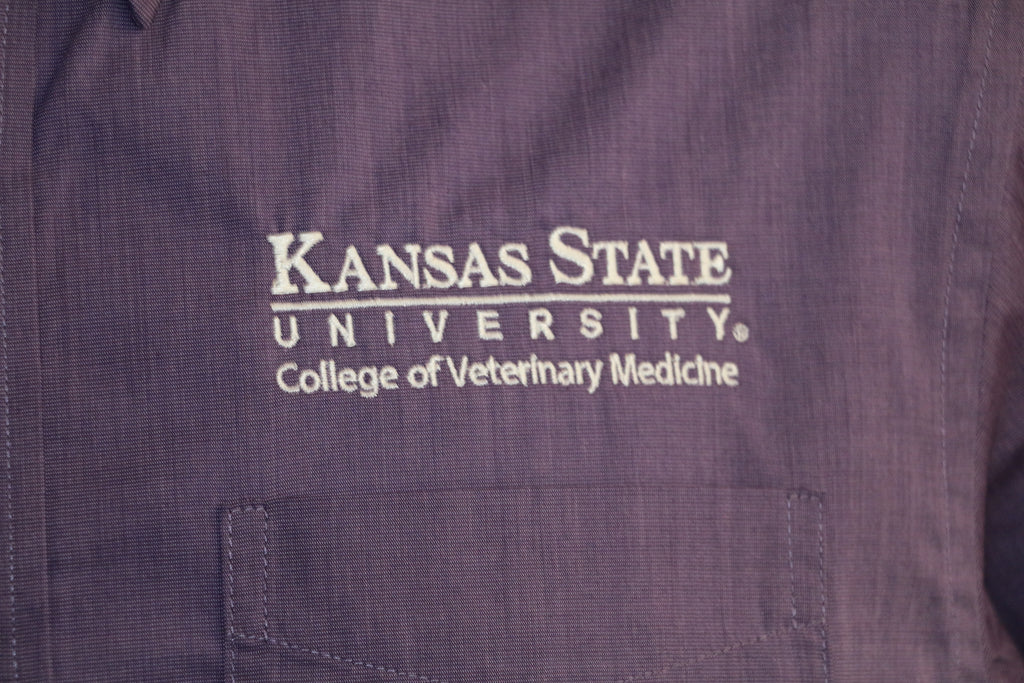 A close-up of the customized Port Authority Purple Woven long sleeve dress shirt white K-State logo. 