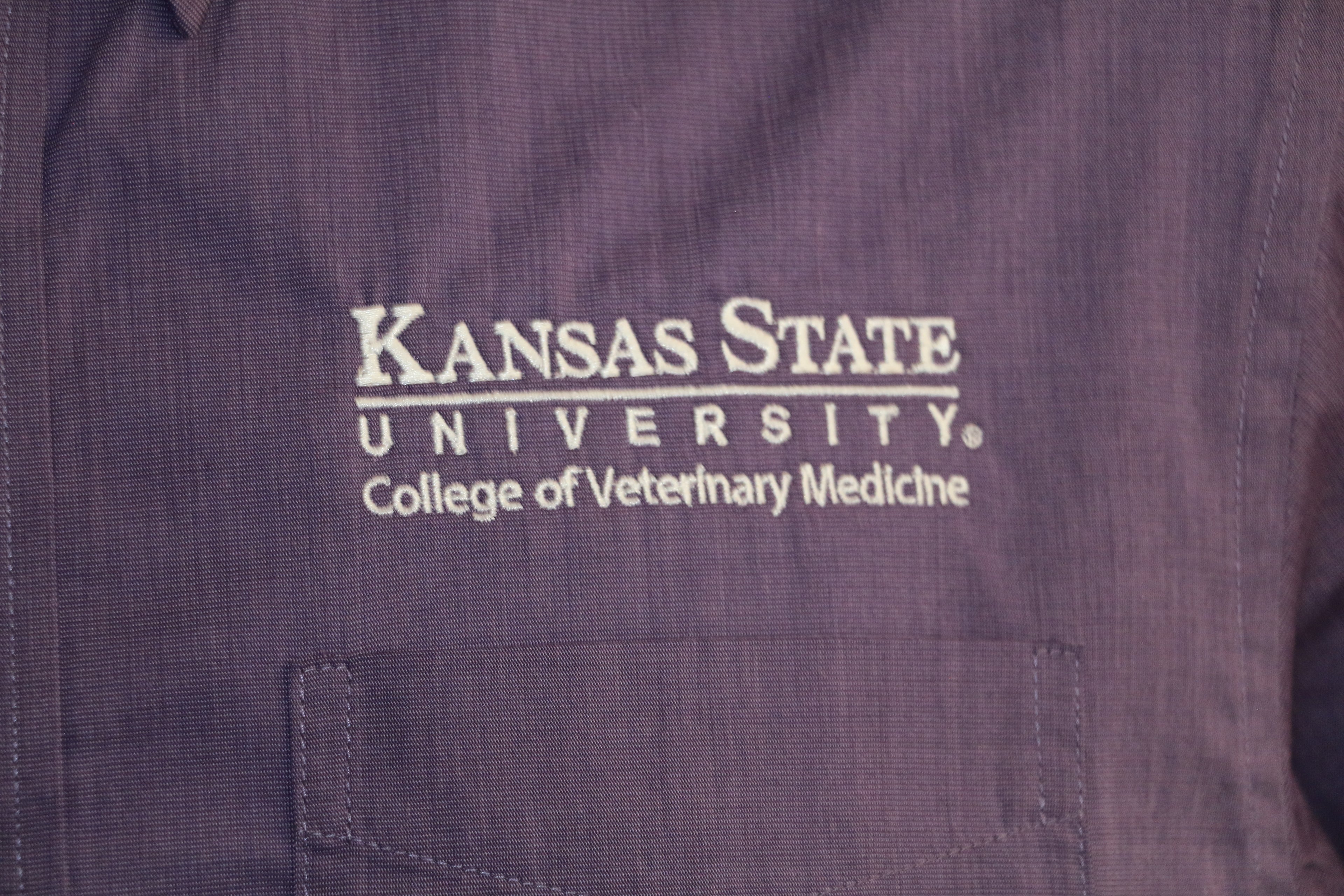 A close-up of the customized Port Authority Purple Woven long sleeve dress shirt white K-State logo. 
