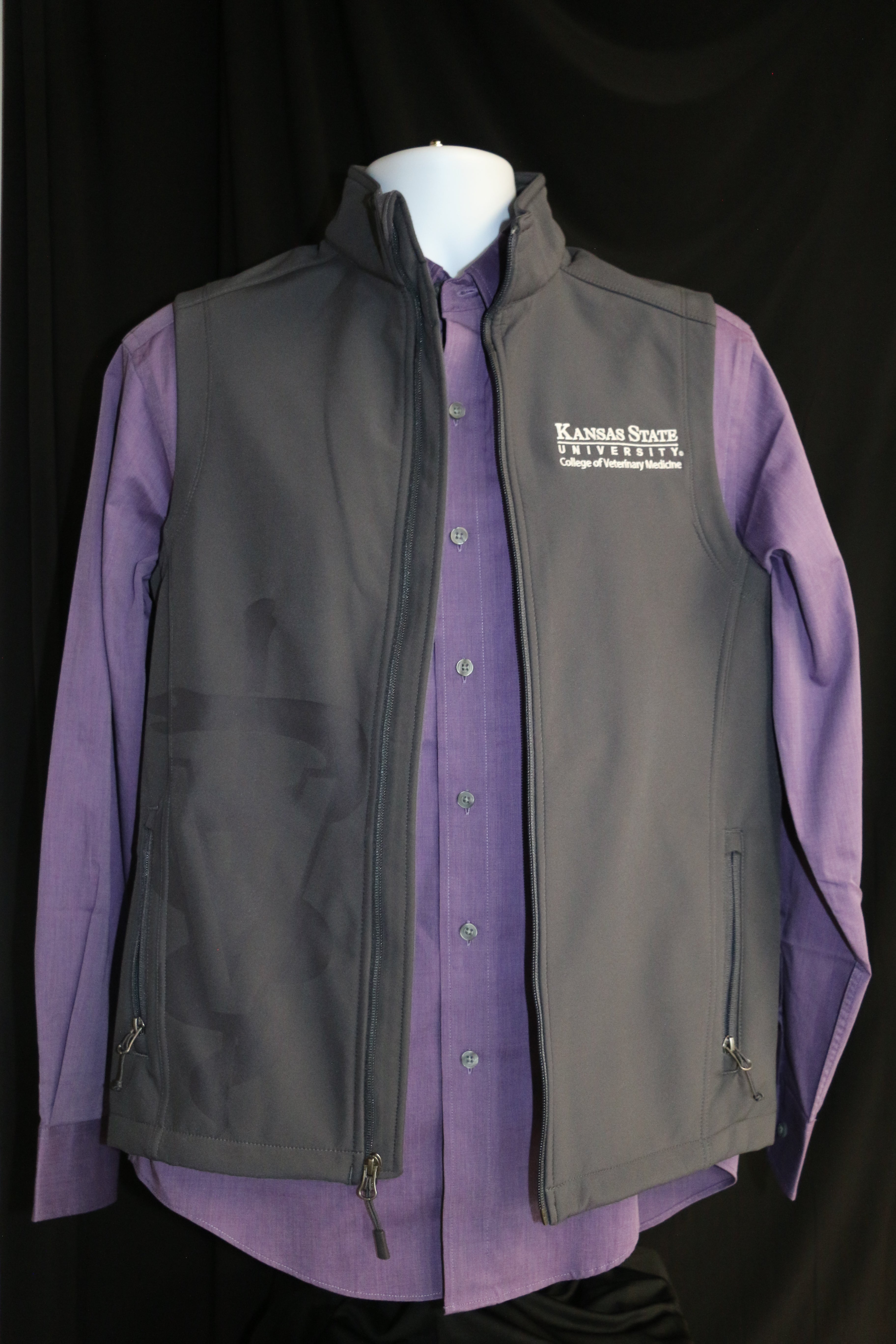 Men's gray soft-shell vest with laser etched Caduceus symbol, displayed over a purple shirt. The vest features zipper pockets and a white CVM logo on the upper left side. 