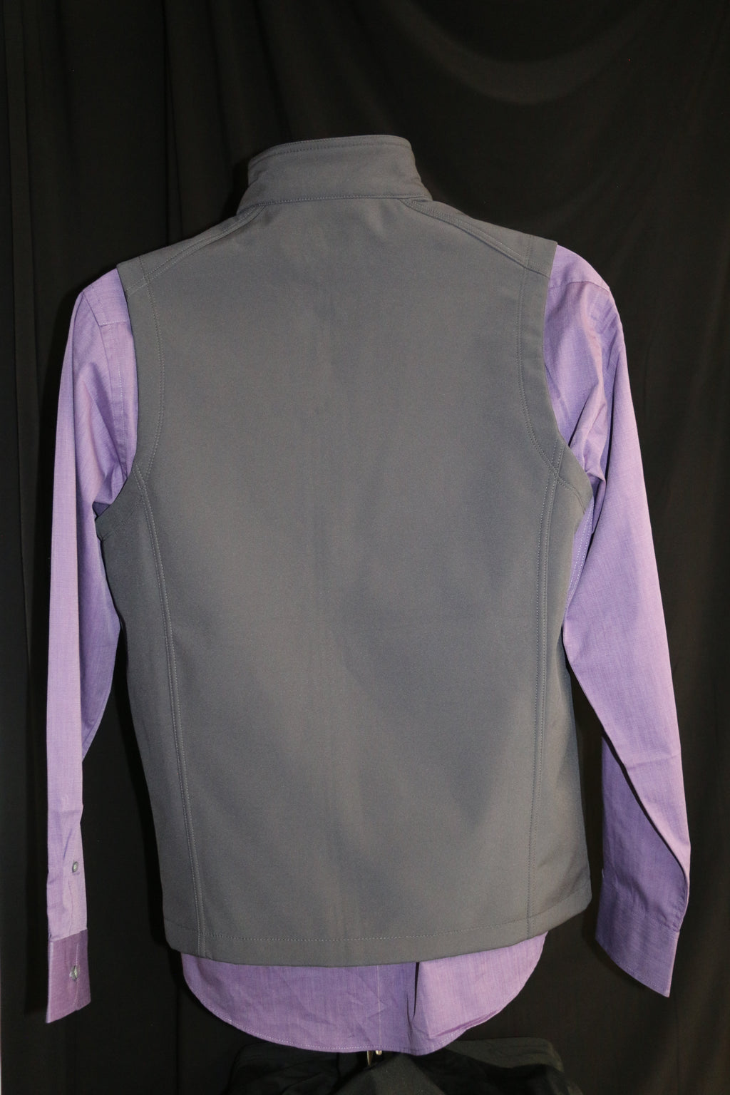 A rear view of the Men's gray soft-shell vest with laser etched Caduceus symbol, displayed over a purple shirt. The vest features zipper pockets and a white CVM logo on the upper left side. 