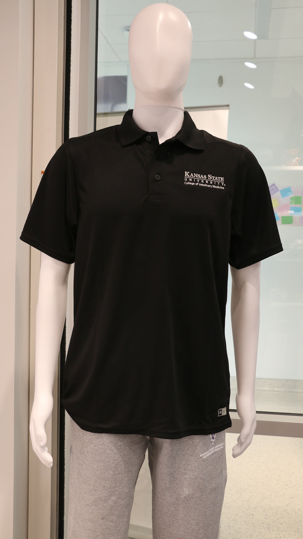 A black Russell Athletic polo shirt with a white CVM logo displayed on a mannequin.