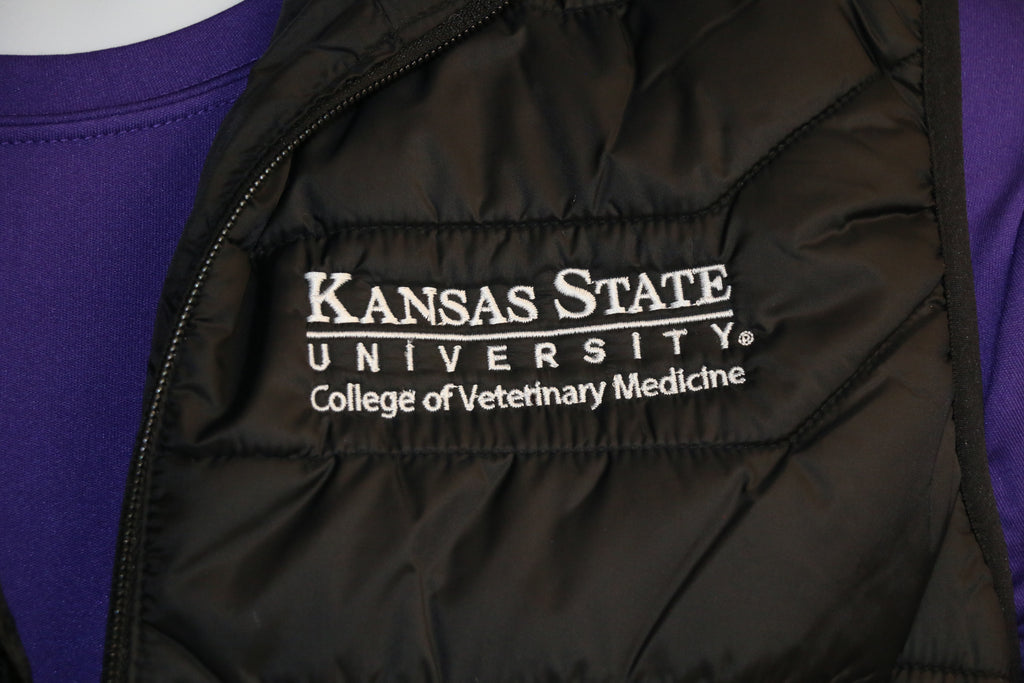 A close-up of the white "Kansas State University College of Veterinary Medicine" logo on the upper left side of the puffer vest. 
