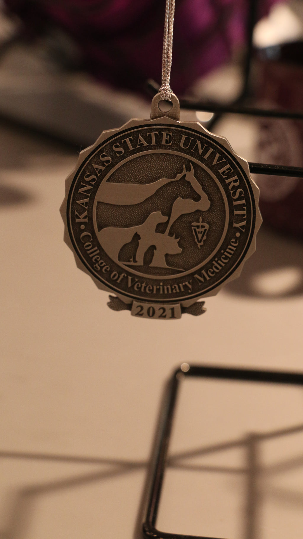 A pewter Christmas ornament with a university logo and the year 2021 inscribed on it, displayed on a chain.