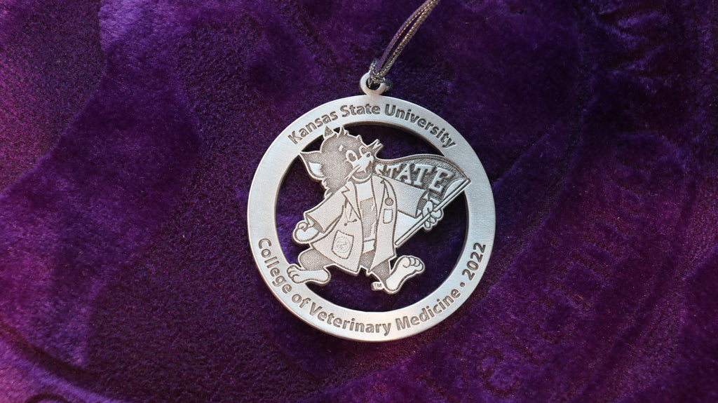 A pewter Christmas ornament featuring Labcoat Willie and text that reads 'Kansas State University College of Veterinary Medical 2022'.