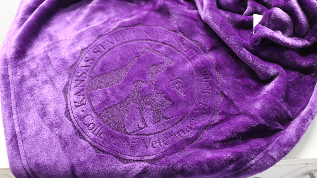 A purple plush blanket with a laser etched logo in the center.