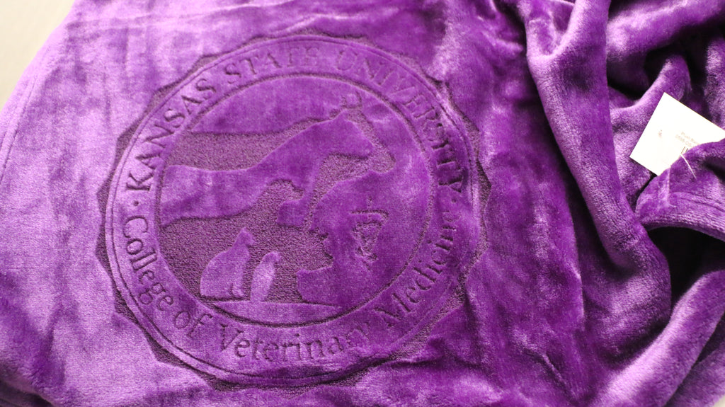 A purple plush blanket with a laser etched logo in the center.