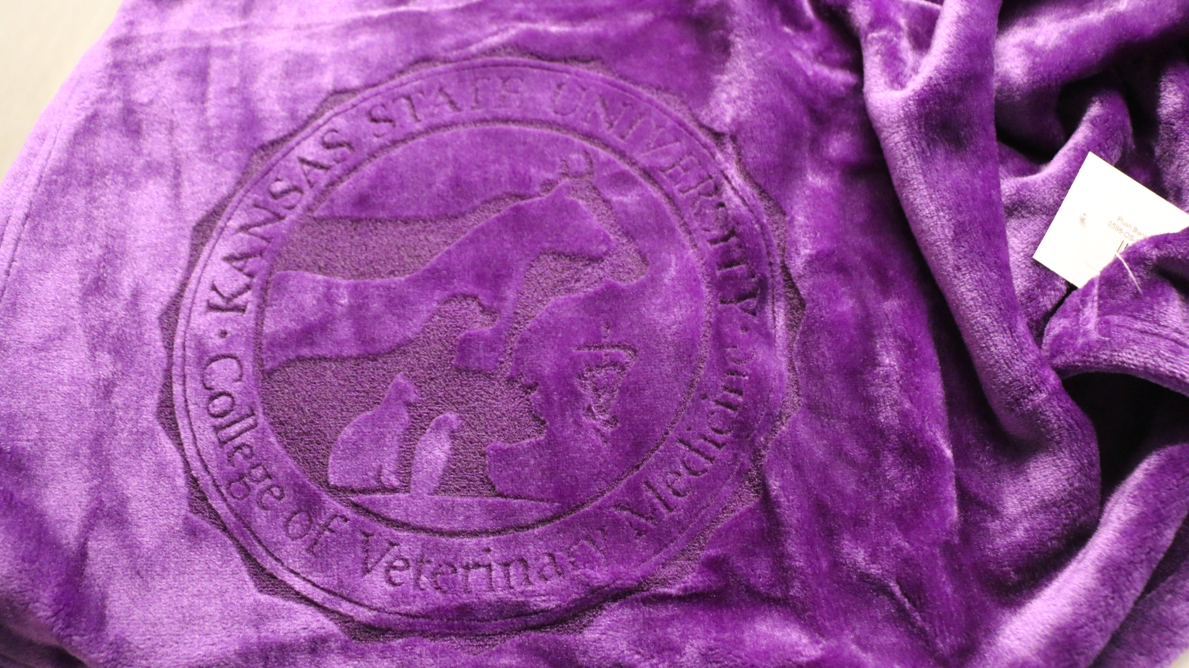 A purple plush blanket with a laser etched logo in the center.