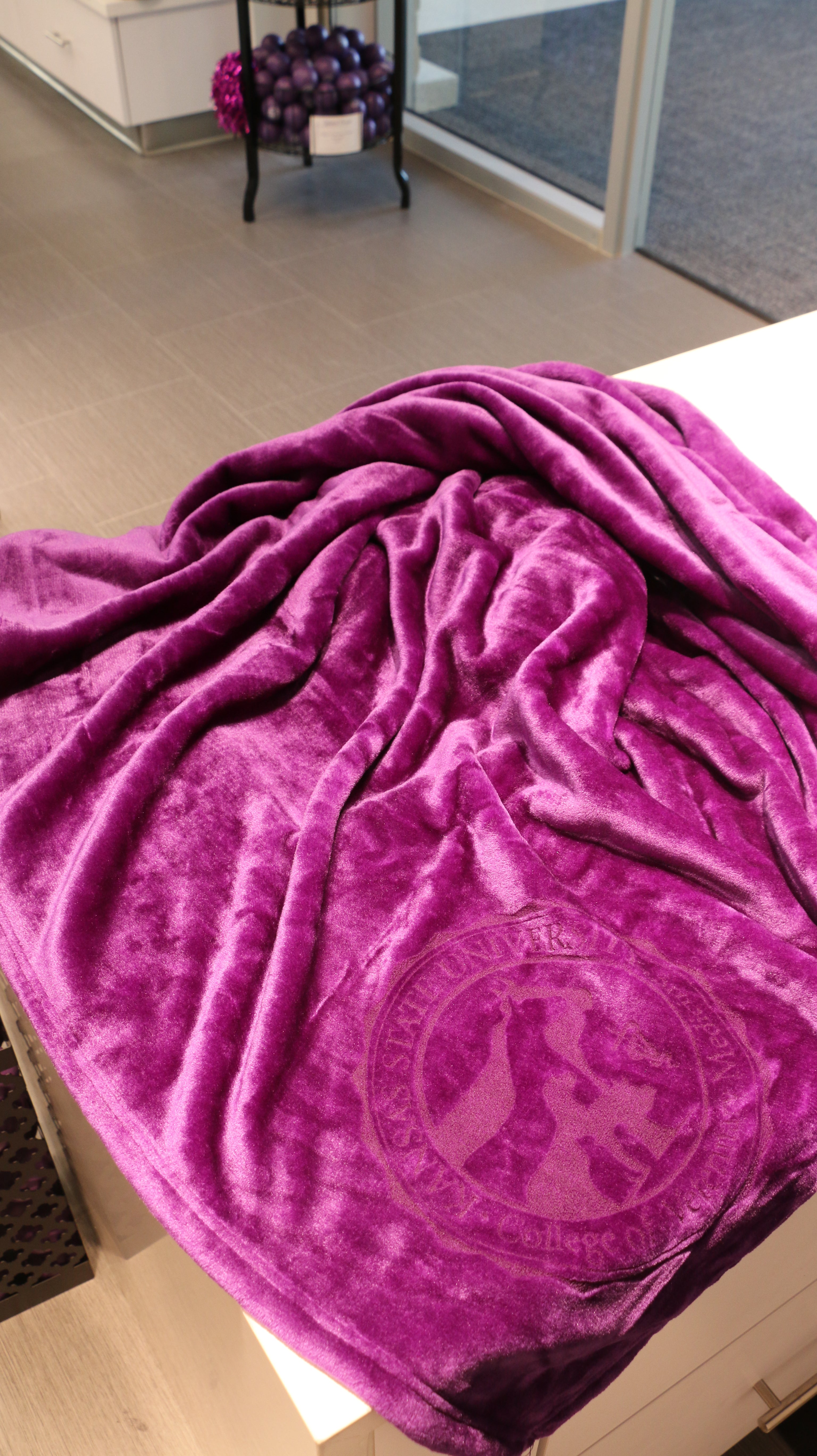 A purple plush blanket with a laser etched logo in the bottom left hand corner.