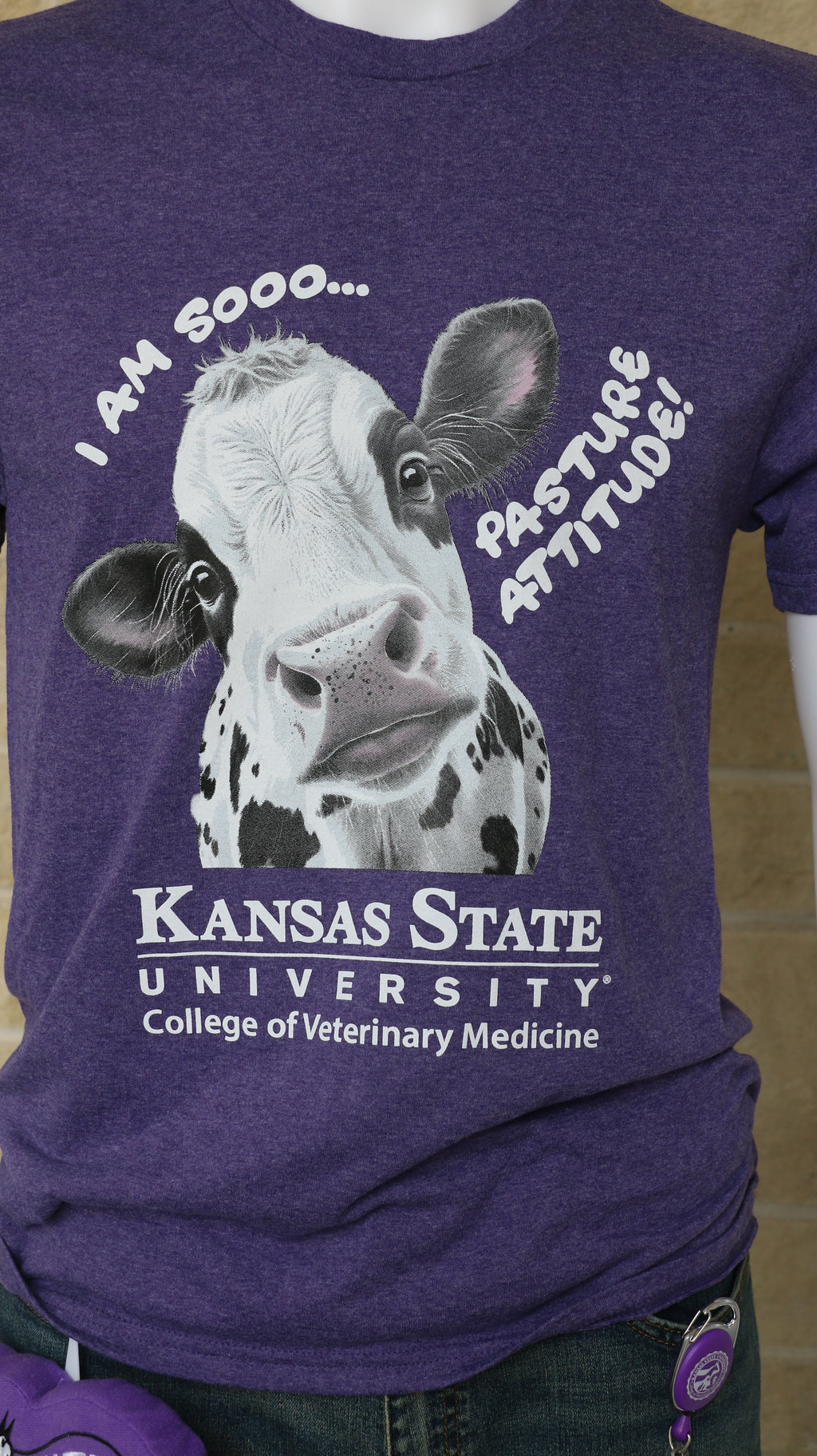 A mannequin wearing a heathered purple Port & Co t-shirt with a graphic of a cow and text that reads "I am sooo... pasture attitude!" with the K-State CVM logo. 