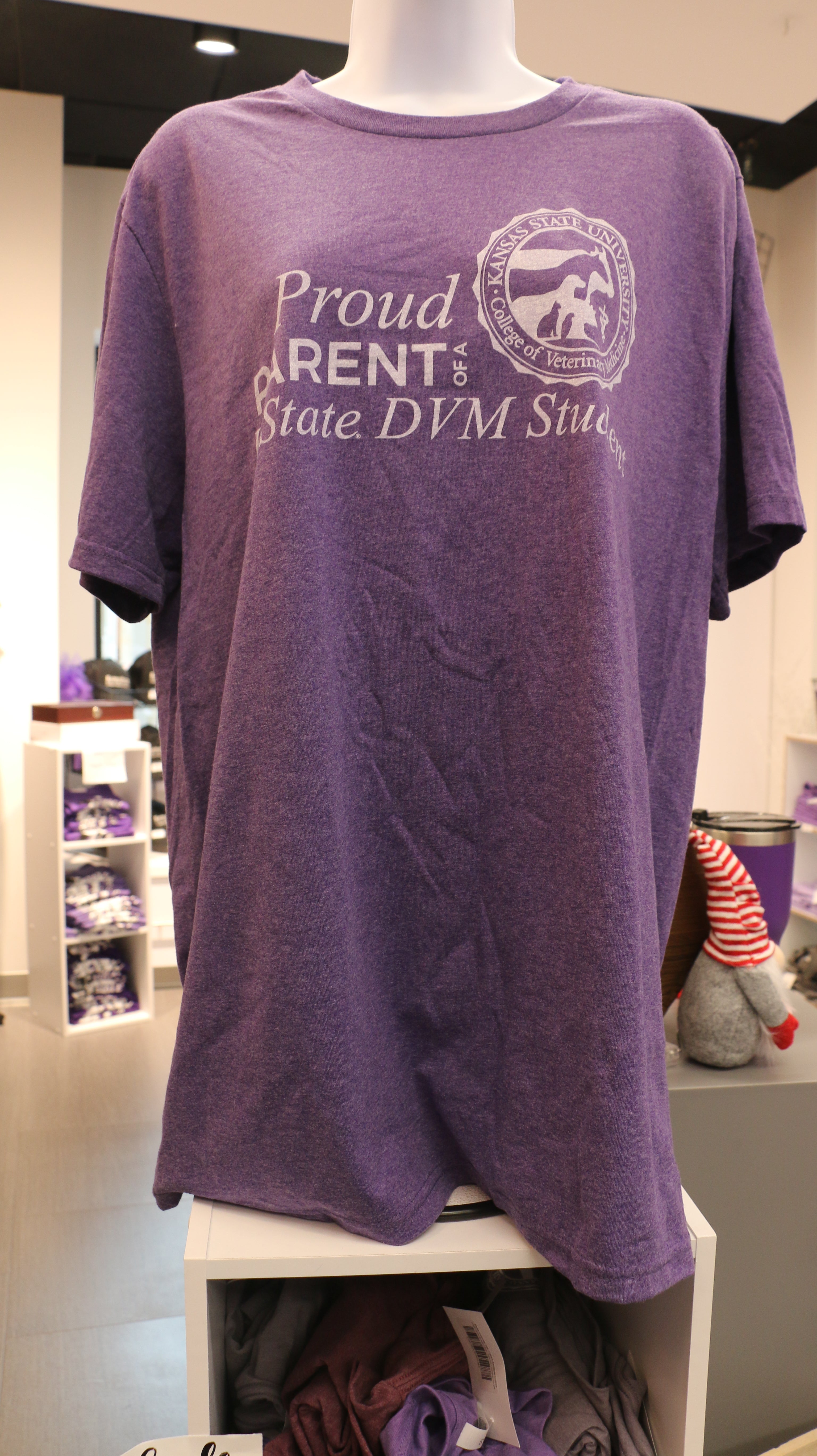 A heather purple Port & Co t-shirt displayed on a mannequin, featuring the text 'Proud Parent of a K-State DVM Student' with the CVM seal.