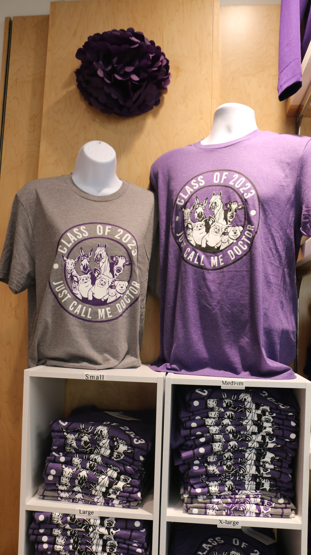 Two graduation t-shirts displayed on mannequins, one in purple and the other in gray, both with 'Class of 2023 Just Call Me Doctor' text and a mixed animal graphic.
