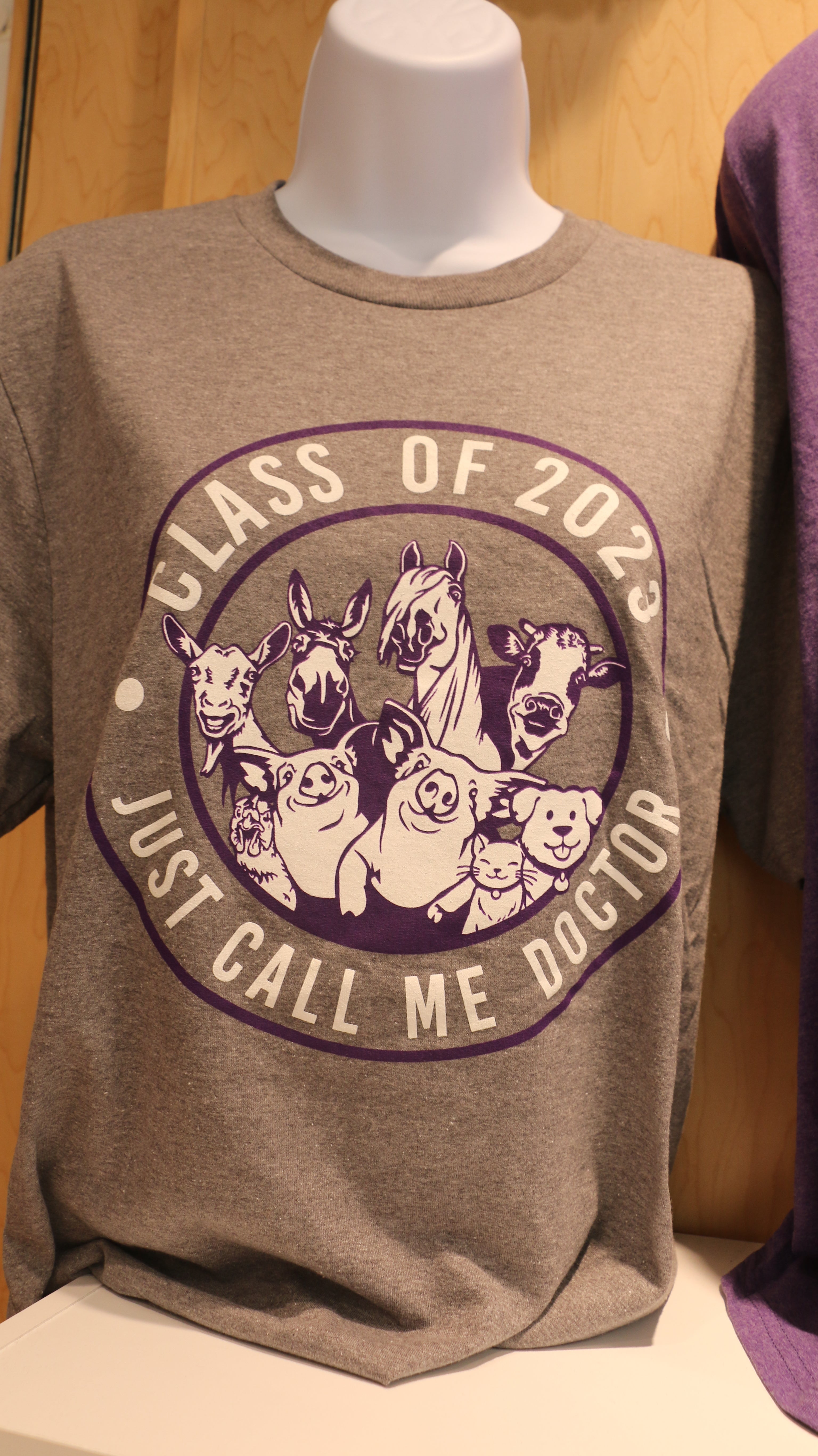 A graduation t-shirt displayed on a mannequin in gray with 'Class of 2023 Just Call Me Doctor' text and a mixed animal graphic.