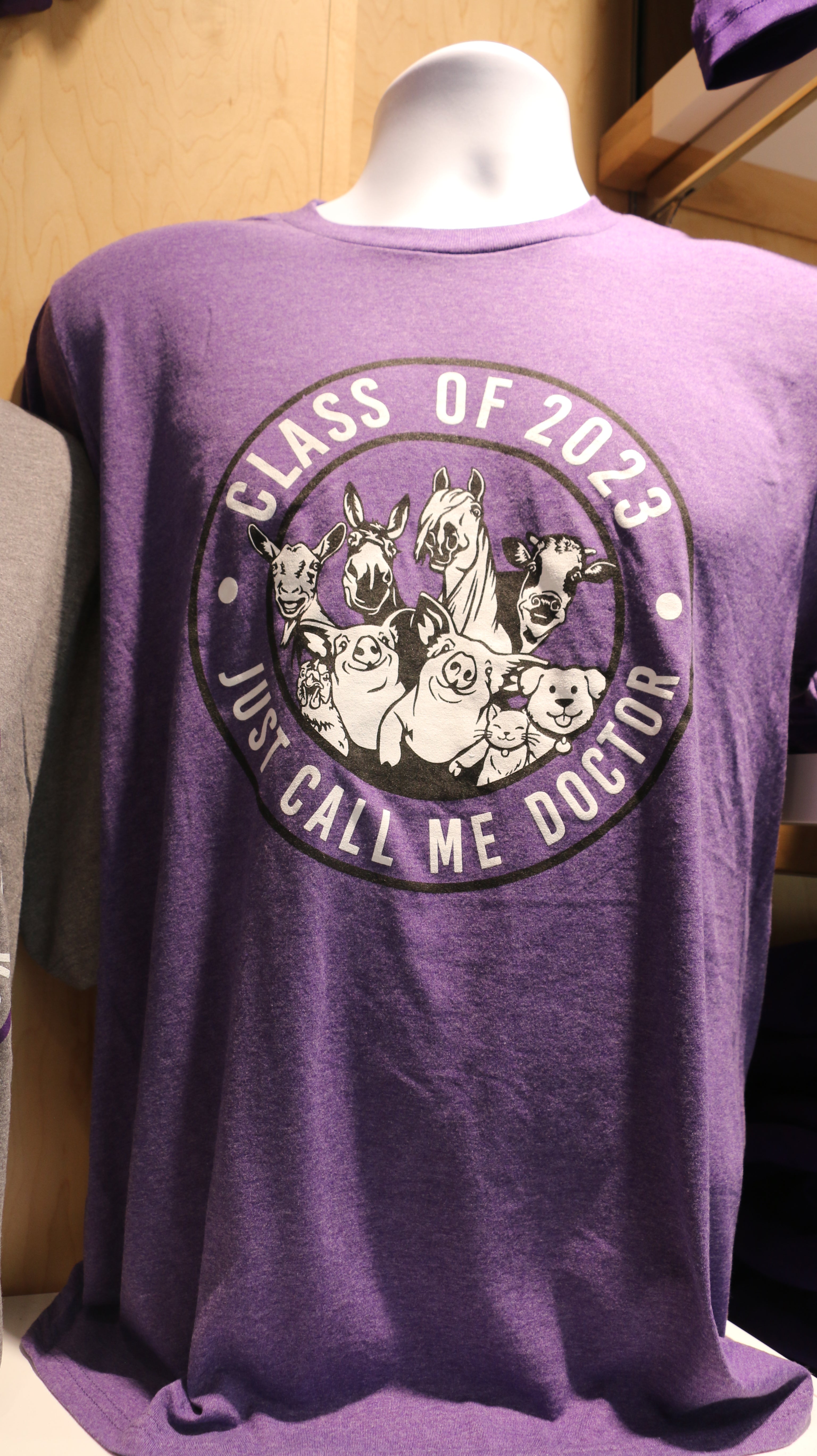 A graduation t-shirt displayed on a mannequin in purple with 'Class of 2023 Just Call Me Doctor' text and a mixed animal graphic.