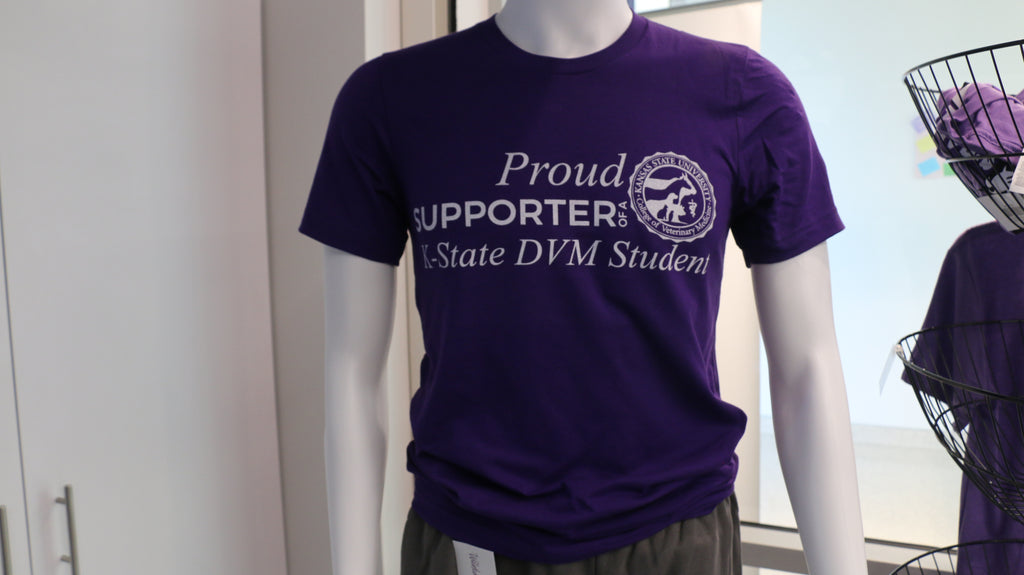 A purple Bella canvas T-shirt displayed on a mannequin, with the text 'PROUD SUPPORTER OF A K-STATE DVM STUDENT' printed on the front.