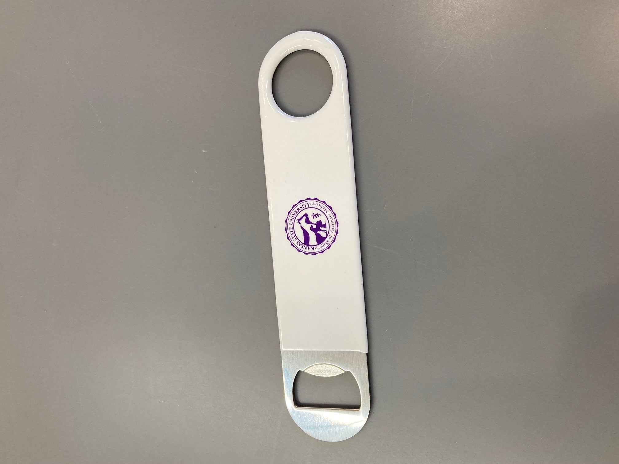 Stainless steel pub style bottle opener with a vinyl wrapped handle and purple CVM logo in the center. 
