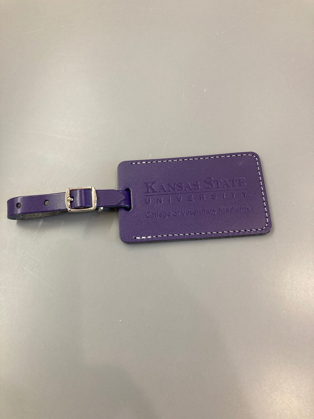 A purple leather luggage tag with a buckled strap and embossed text 'Kansas State University College of Veterinary Medicine'.