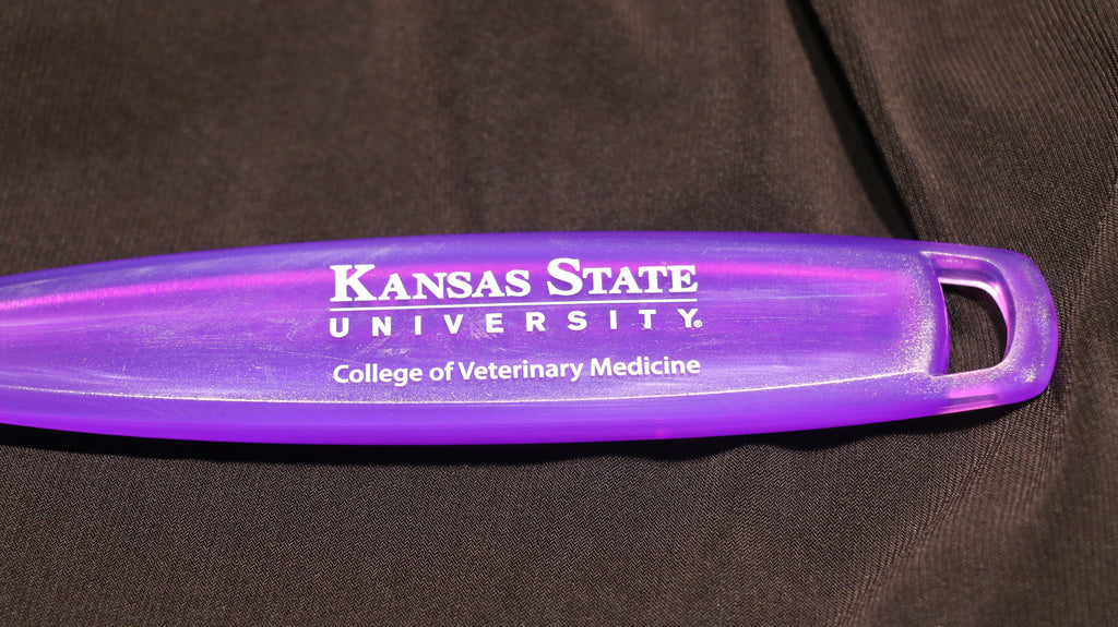 A purple silicone spatula with a translucent handle, white CVM logo, and lying on a black surface.