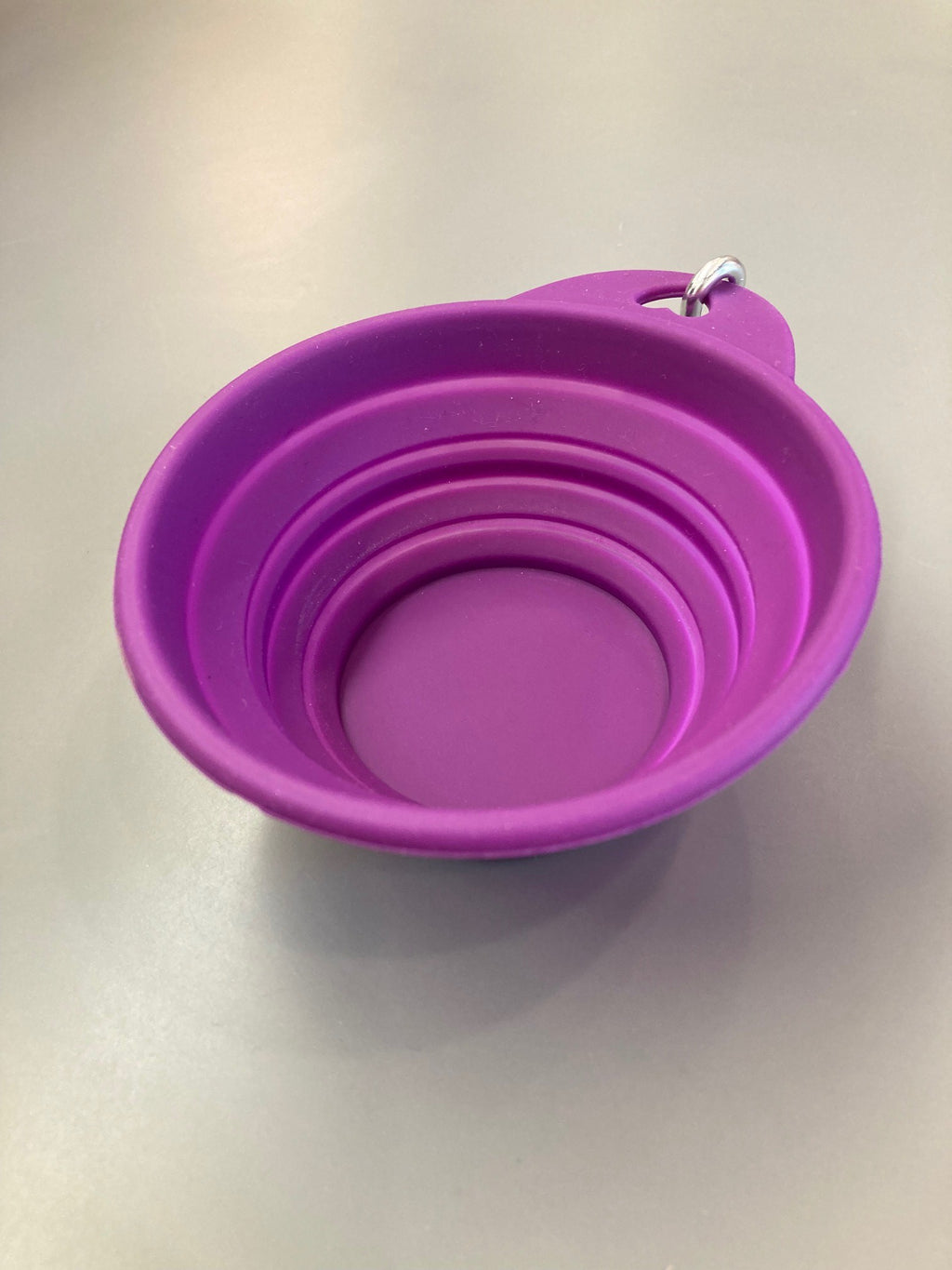 A purple collapsible silicone pet bowl with a clip for attaching to a leash or belt buckle.
