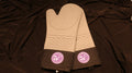 A pair of silicone oven mitts with a light grey base color and black fabric cuffs. On the center of each cuff on the mitt there is a white and purple CVM seal. 