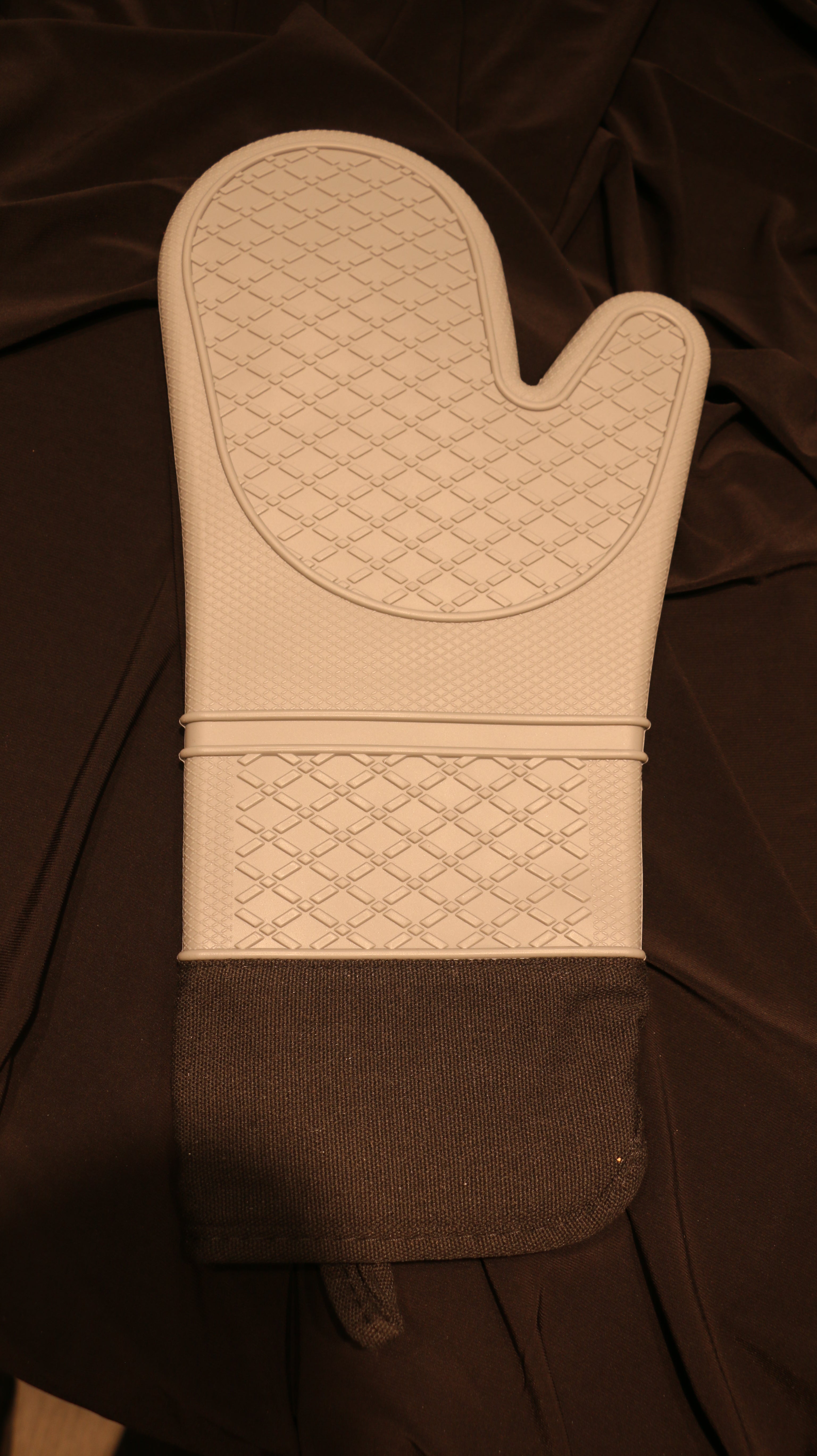 A rear view of a silicone oven mitt with a light grey base color and black fabric cuff.